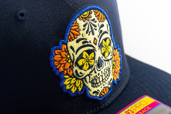 Club America Day of the Dead Snapback Hat with floral skull embroidered on the front, Club America embroidered on the side, "Dia de Muertos" embroidered on the back. The hat has a high crown, flat peak brim, and a snapback closure.